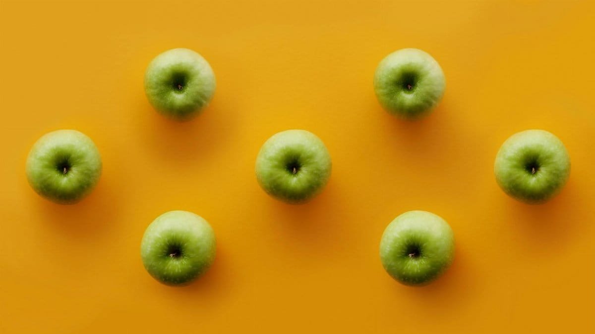 Green apples displayed on a vibrant orange surface, perfect for food-themed projects.