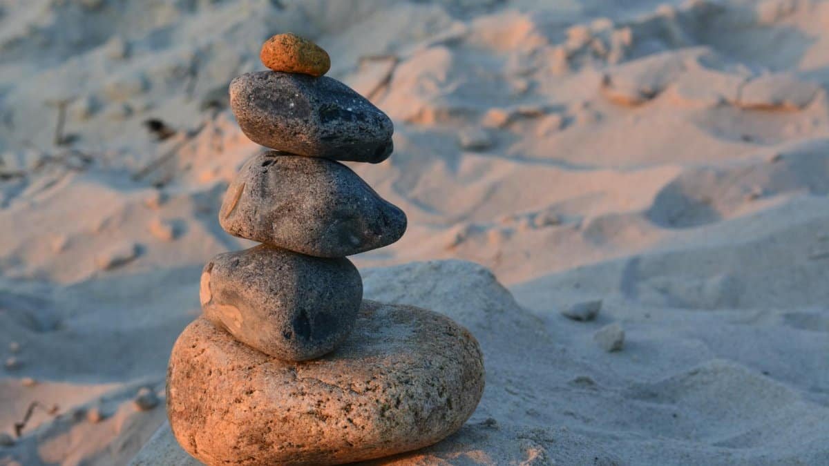 Close-up of a balanced stone cairn on a sandy beach with warm sunset lighting.