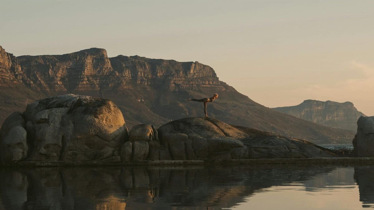 Woman practicing yoga on boulders during sunset in Cape Town, reflecting a serene wellness moment.