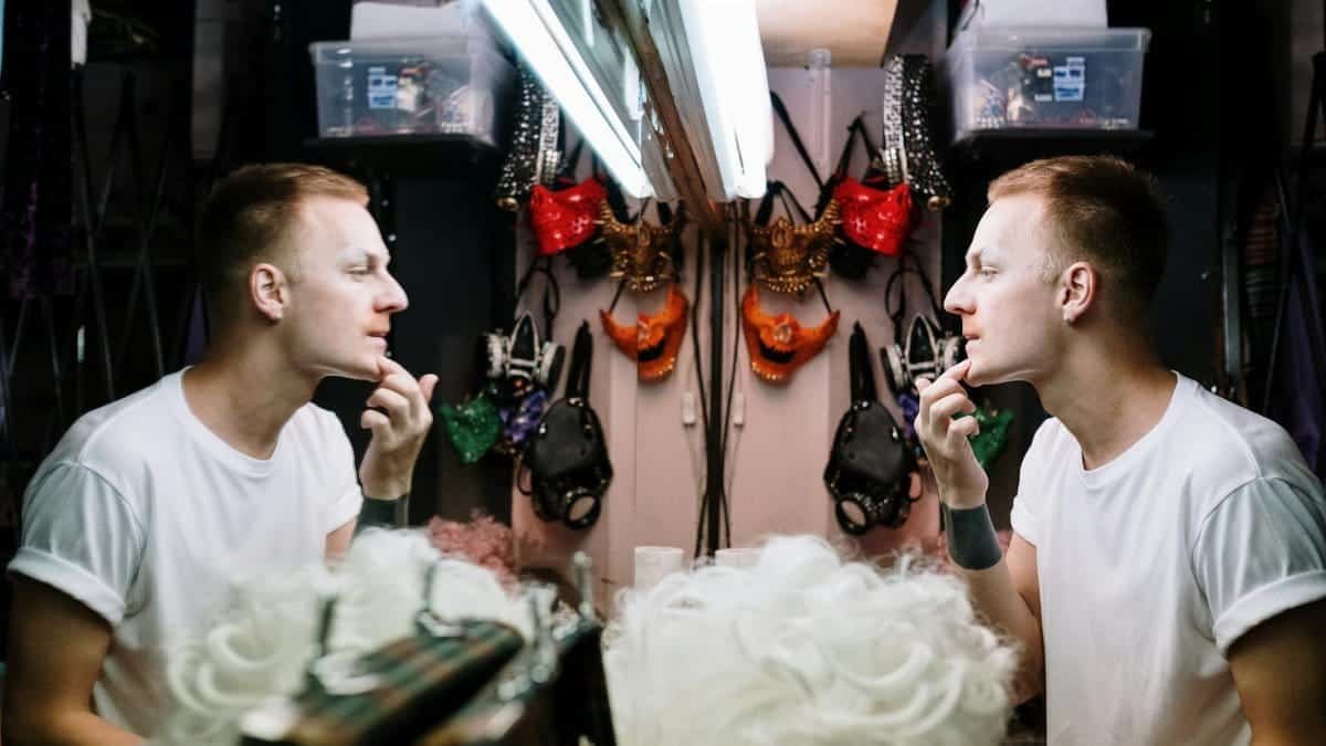 A man preparing for a performance by applying makeup in a dressing room mirror.