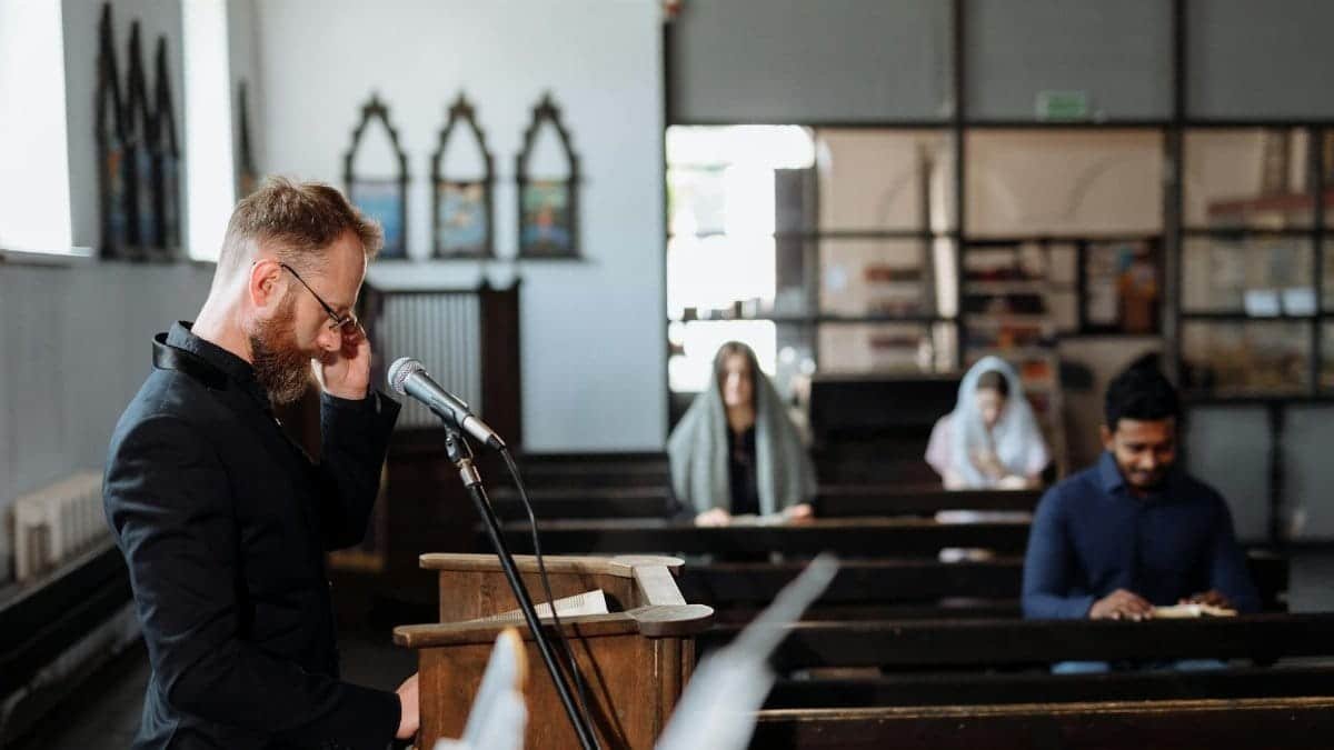 A pastor leads a prayer with congregants seated in a church.