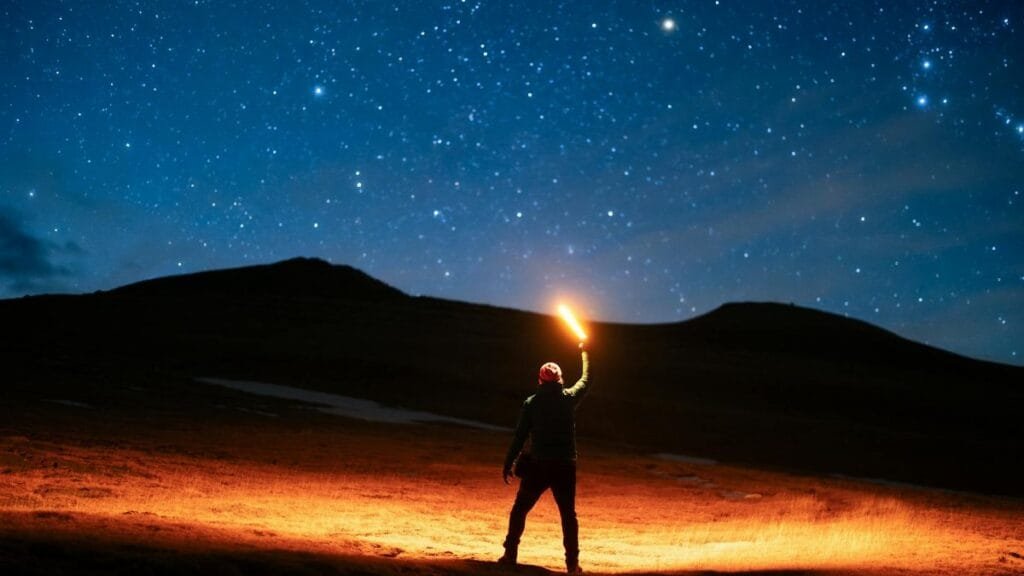 A lone hiker holding a lantern illuminates the night sky filled with stars, creating a magical scene.