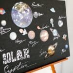 A creatively designed solar system poster displayed on an easel in a classroom setting via Pexels