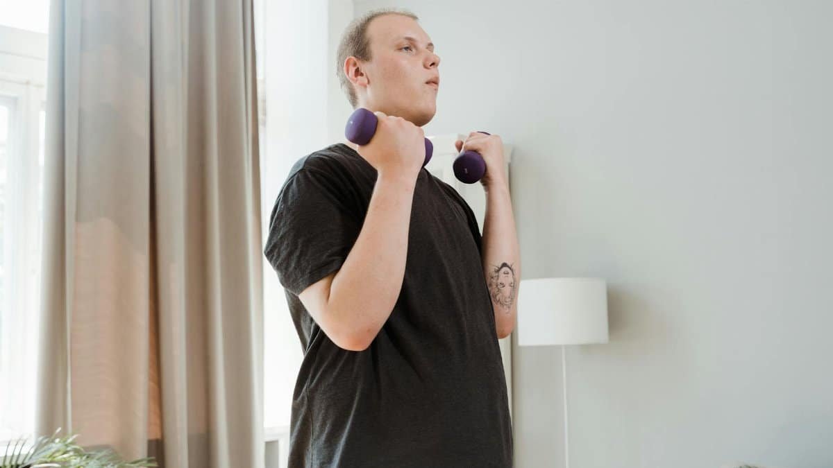 A young man lifting dumbbells in a home setting, focusing on personal fitness and health.