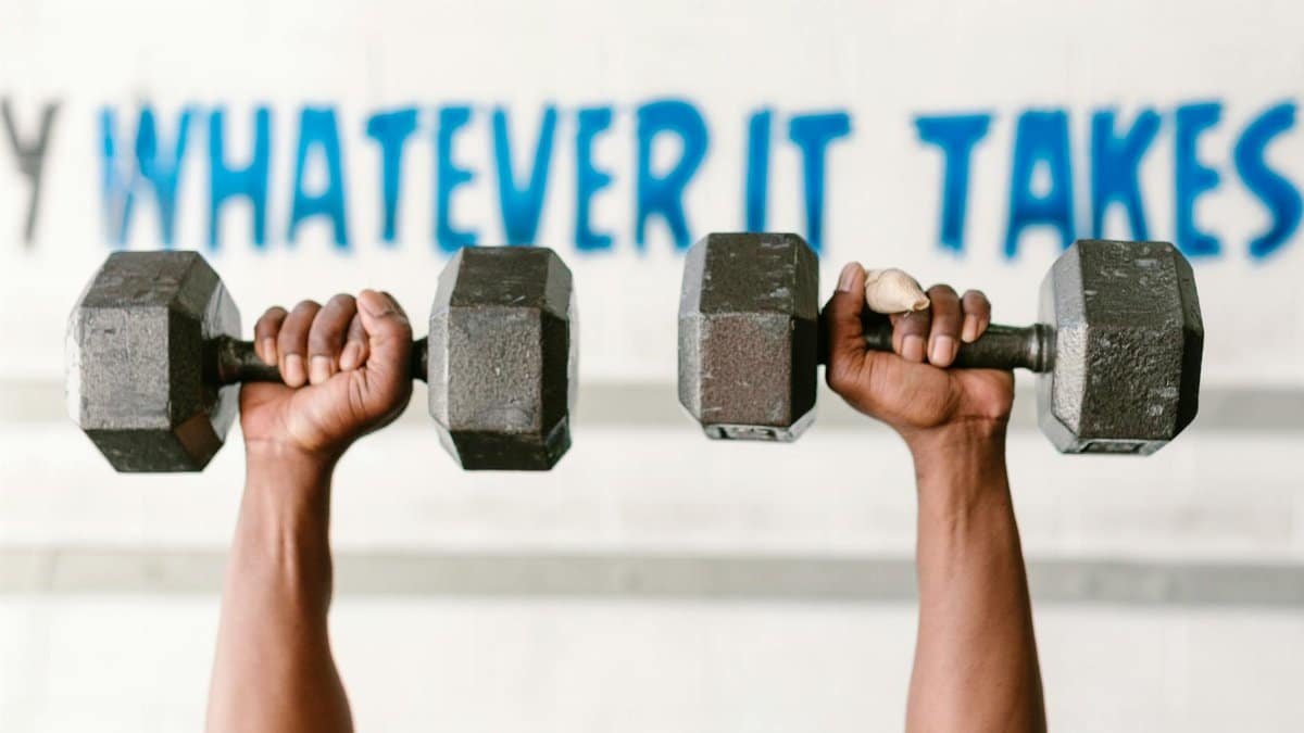 Hands holding dumbbells against motivational text "Whatever It Takes" in a gym setting.