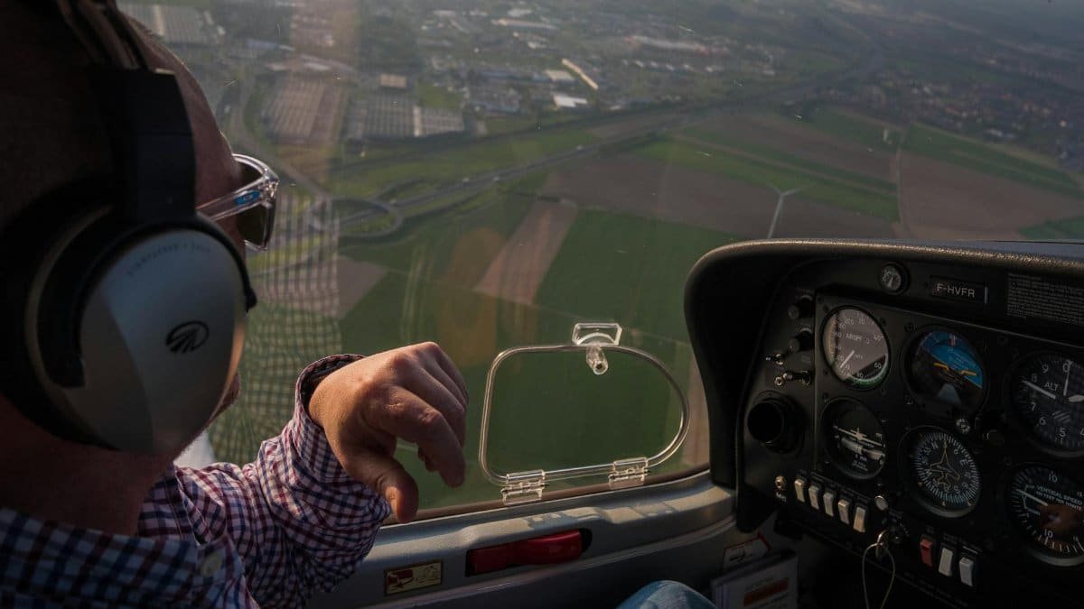 Pilot in cockpit with aerial view of fields in Hauts-de-France, France.