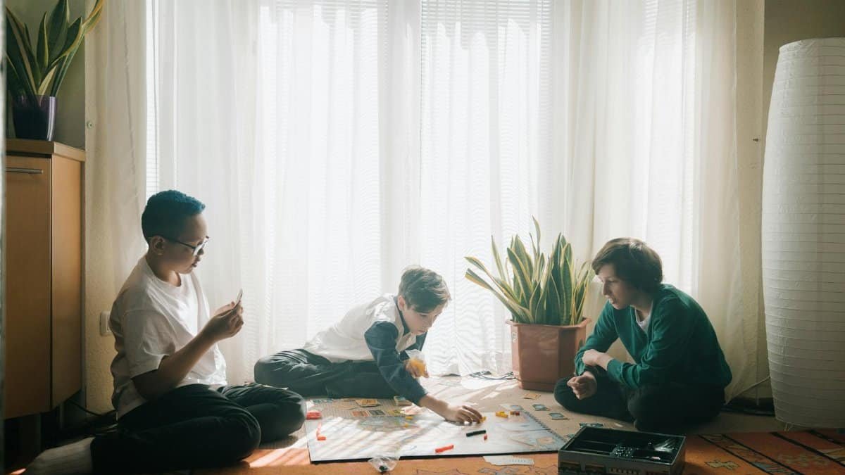 Three teenagers engaged in a strategic board game in a sunlit living room, fostering teamwork and fun.