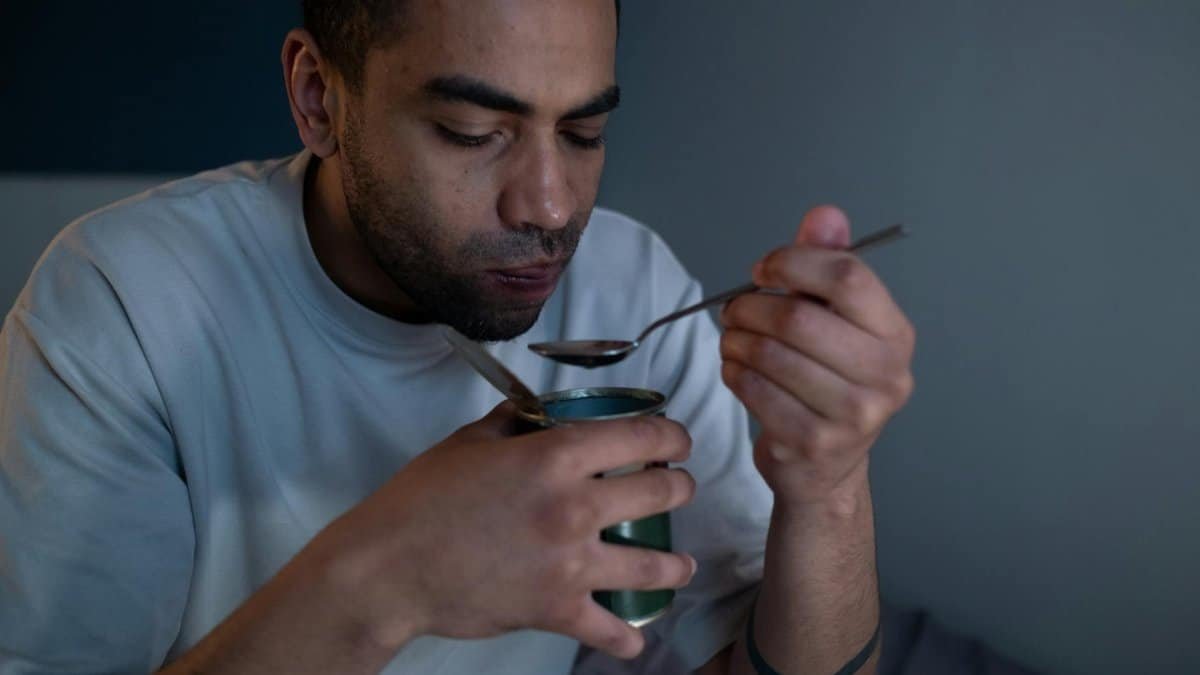 A man enjoys a meal from a tin can in a softly lit indoor setting.