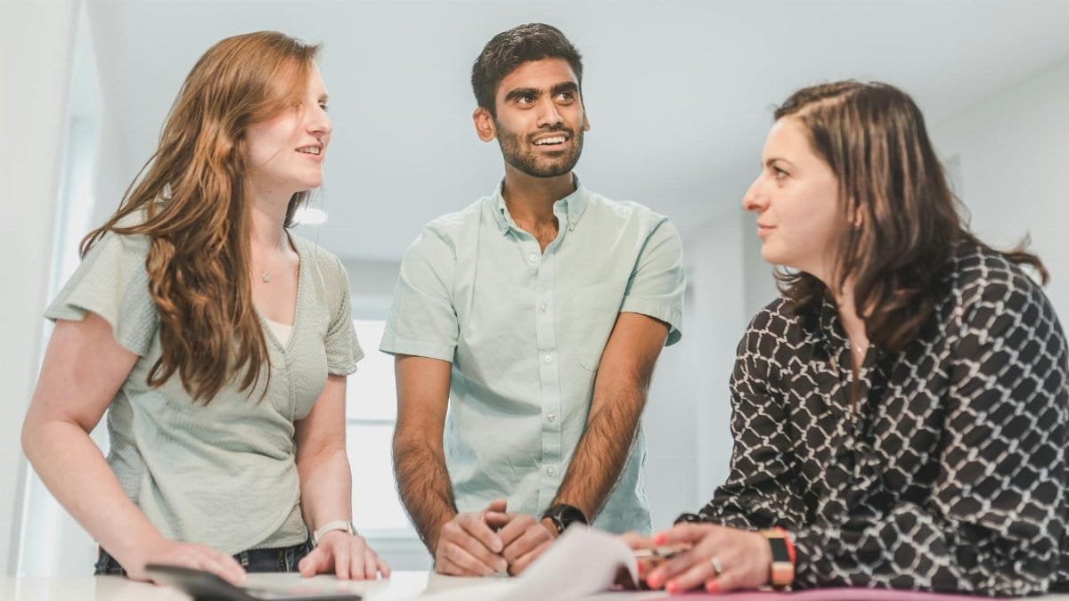 Three diverse adults conversing happily about real estate in a bright indoor setting.