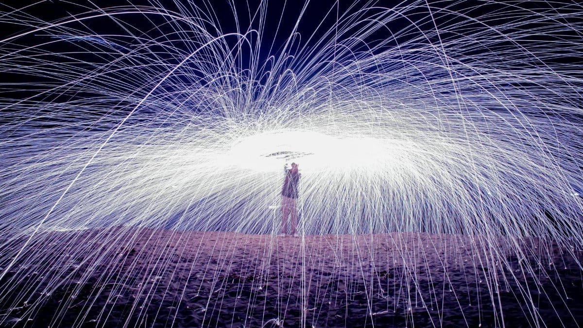 A mesmerizing long exposure of steel wool photography on a beach, creating a shower of sparks.