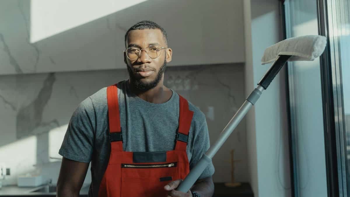 A professional cleaner holding a tool indoors, dressed in red overalls with natural light.