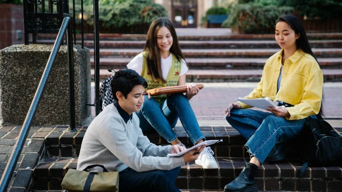 Group of students studying outdoors on college campus steps, enjoying sunny day.