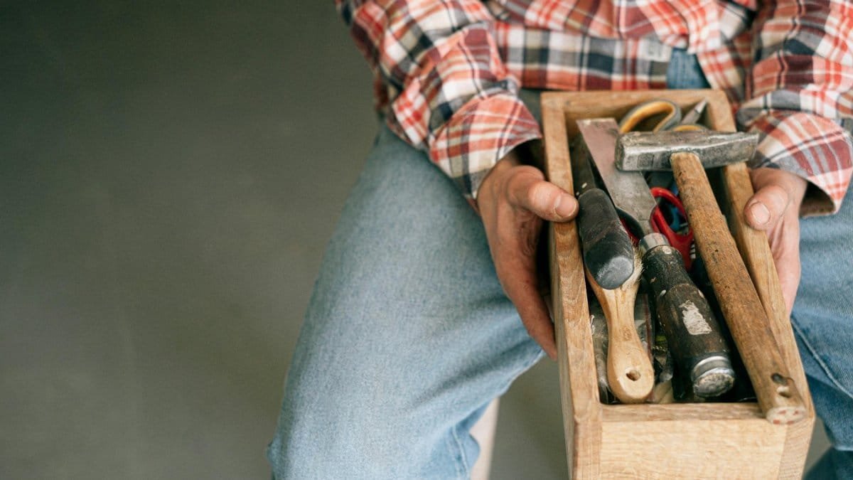A woodworker holding a toolbox filled with essential tools like hammers and screwdrivers.