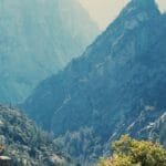A woman practices meditation on a cliff edge, surrounded by majestic mountains and serene nature.