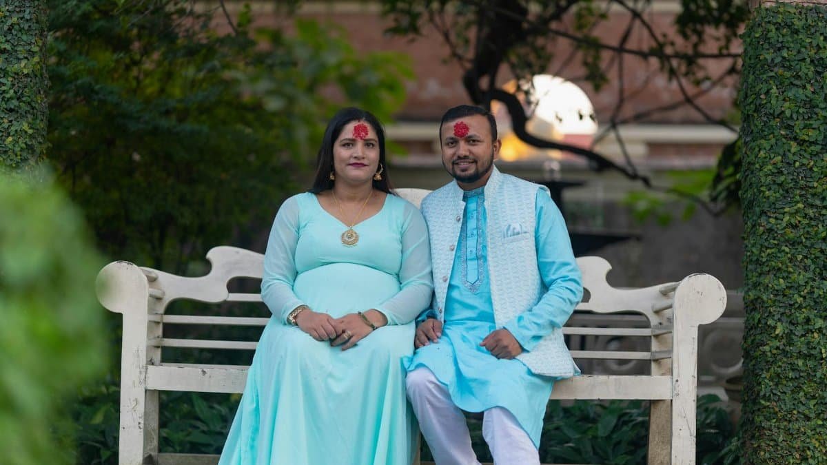 A couple wearing traditional attire seated on a bench in a serene outdoor setting, embodying love and elegance.