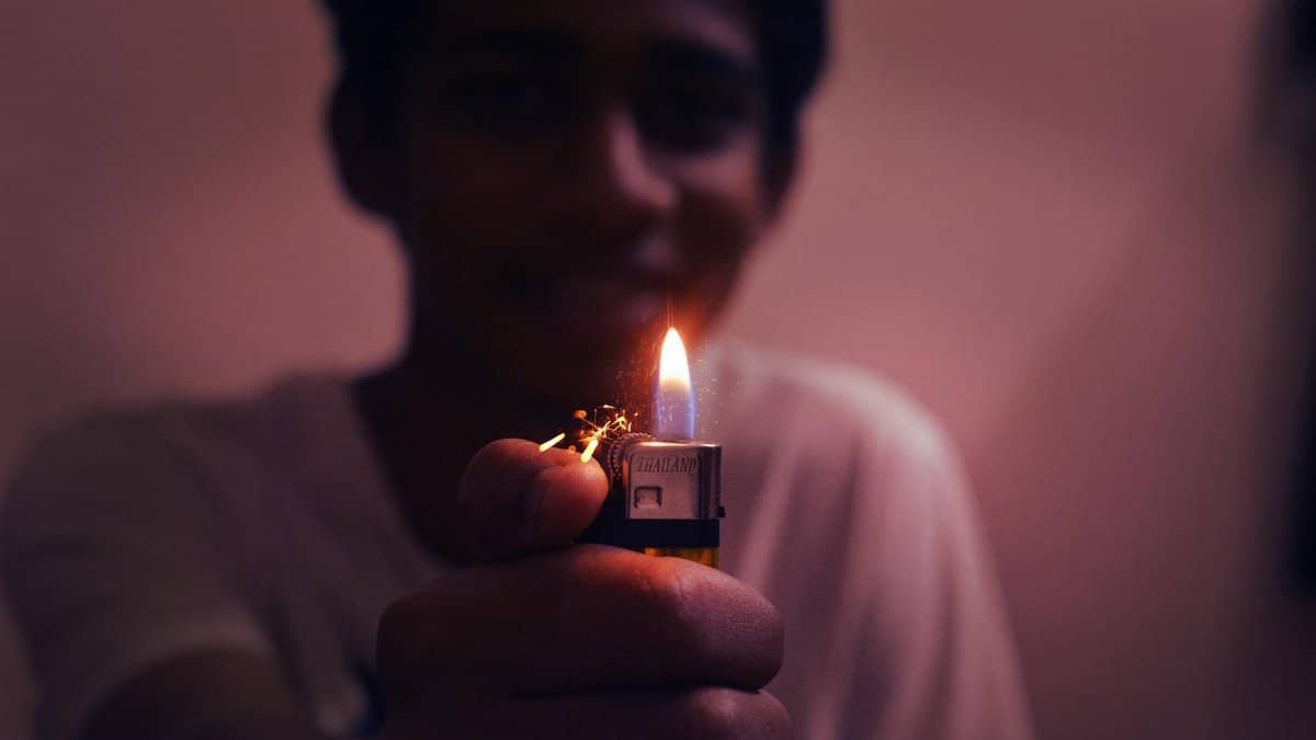 Close-up of a smiling young man lighting a lighter indoors.