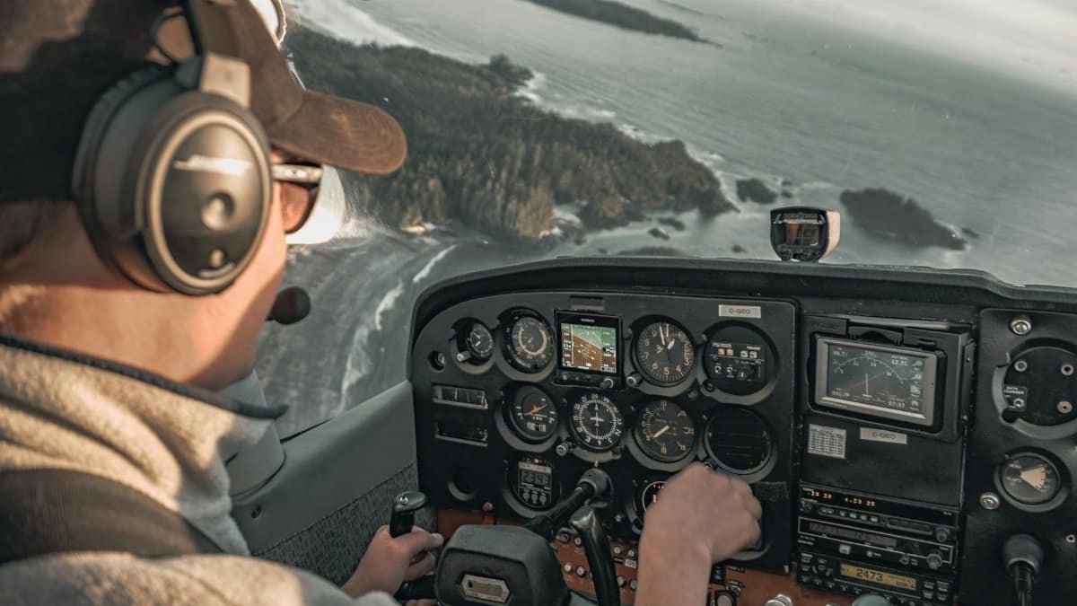Pilot in cockpit flying over a coastal landscape, showcasing the control panel and ocean view.