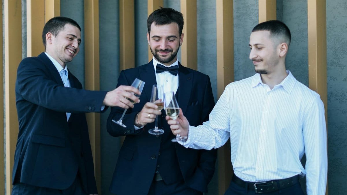 Three men in formal wear toasting with champagne glasses, celebrating outdoors.