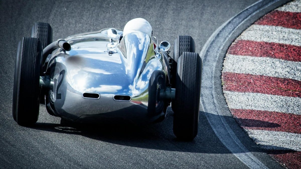A classic silver race car speeding around a track curve, showcasing elegance and speed.