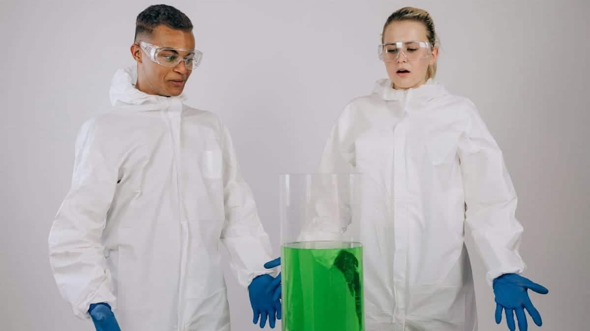 Two scientists in protective gear observing a green chemical experiment in a lab.