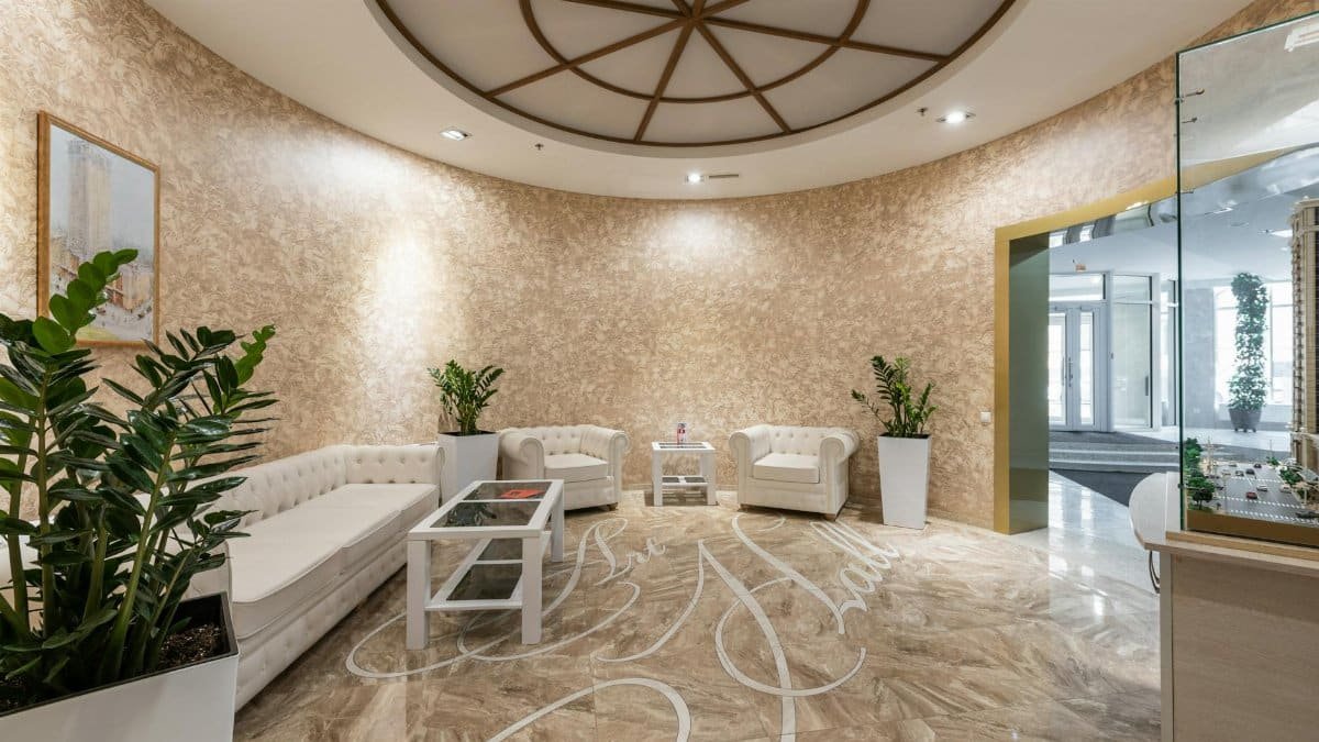 Interior of spacious lobby with comfortable white sofa and armchairs placed in contemporary hotel in daylight
