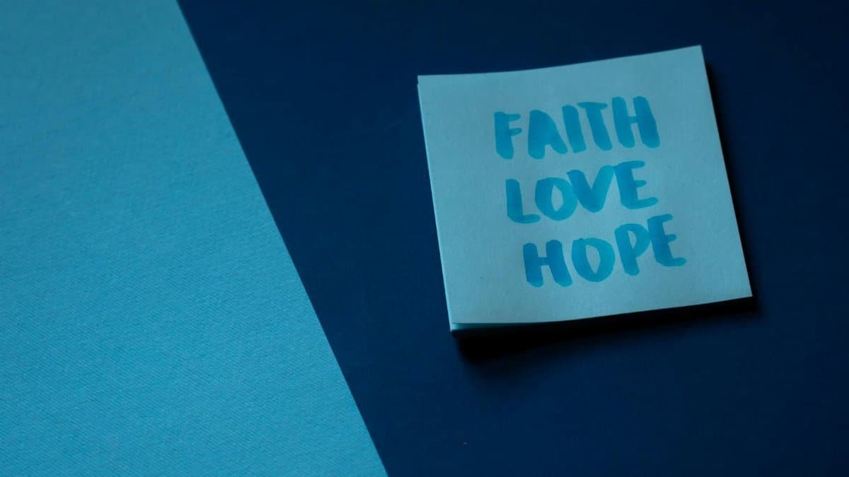 A blue note on contrasting backgrounds displaying the words faith, love, and hope.