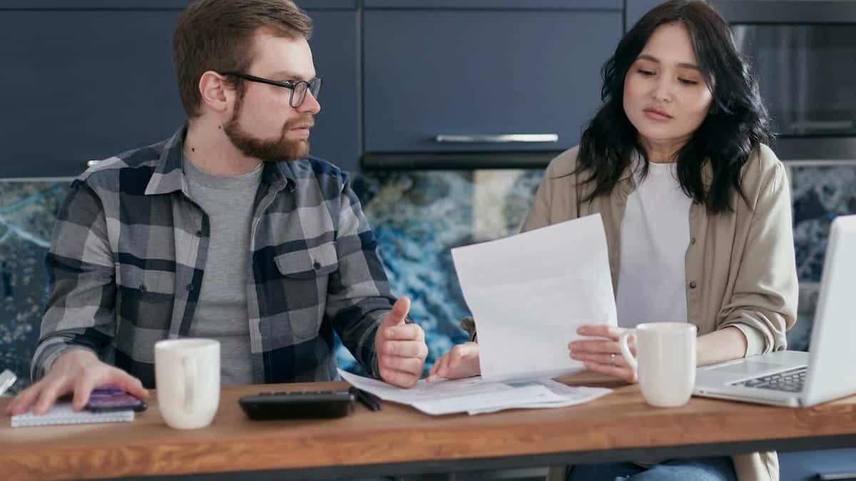 A couple sits at a table reviewing financial documents, looking concerned and focused.