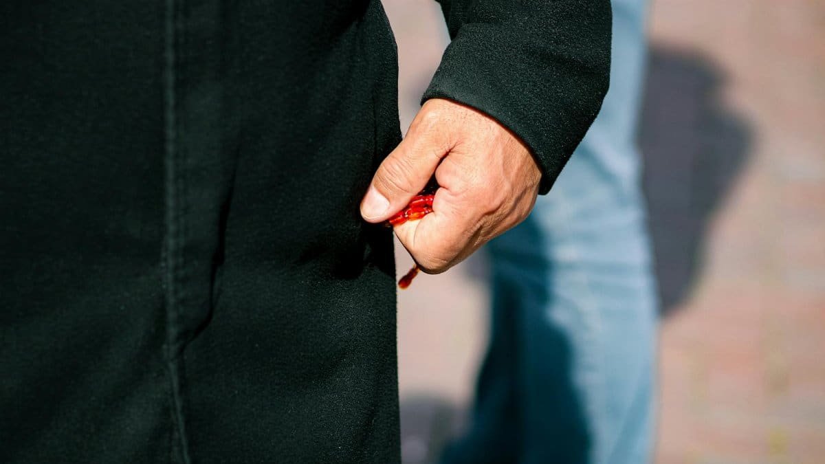 A close-up of a hand holding red rosary beads against a blurred outdoor background.