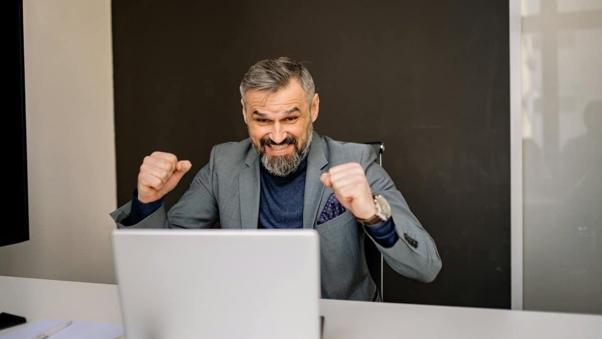Happy businessman celebrating success while looking at laptop in modern office.