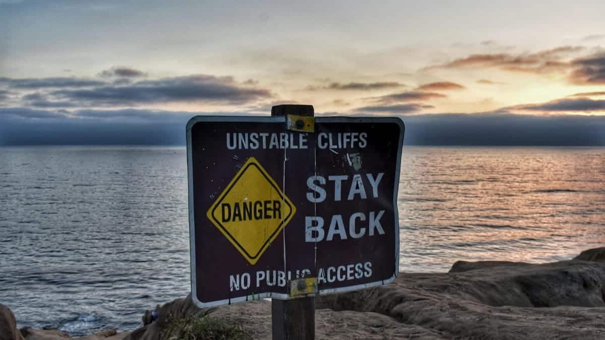 A warning sign on unstable cliffs at sunset by the ocean, capturing a scenic coastal landscape.