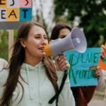 Group of young women passionately protesting for environmental change with signs and a megaphone.