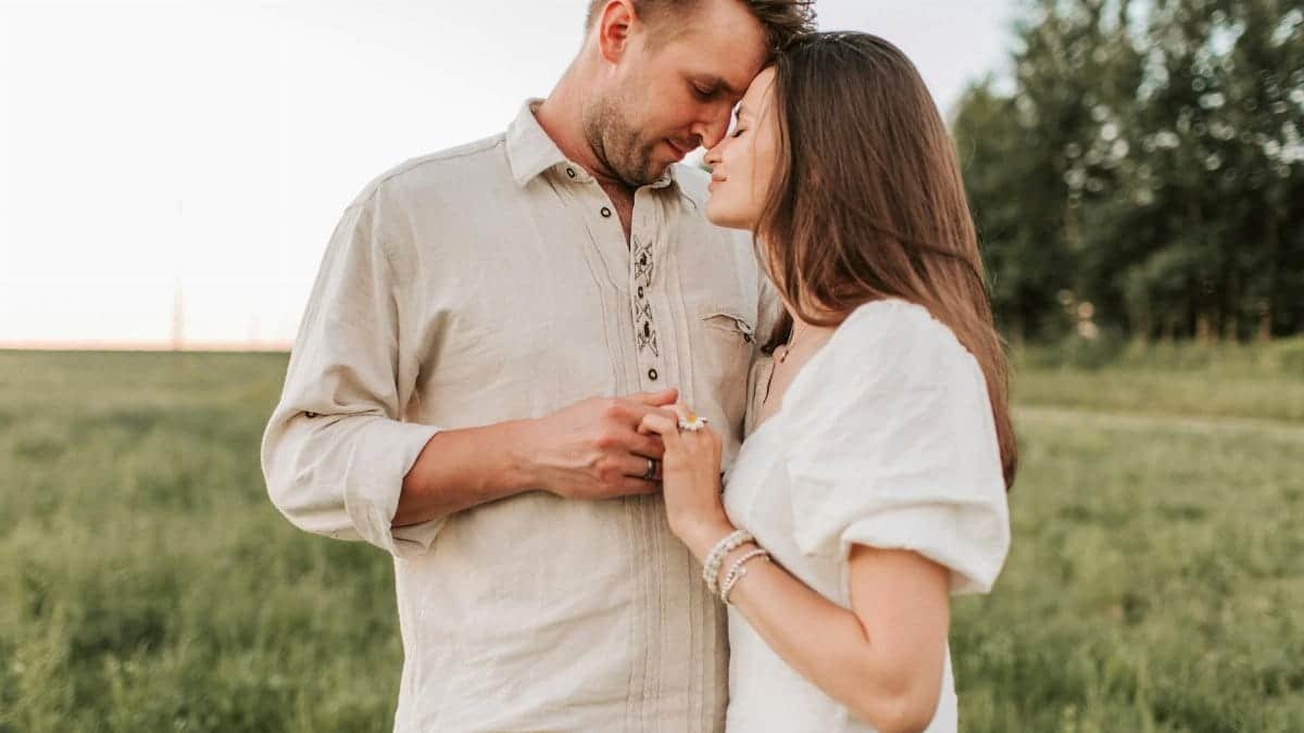 A romantic moment between a couple embracing face to face in a grassy field at sunset.