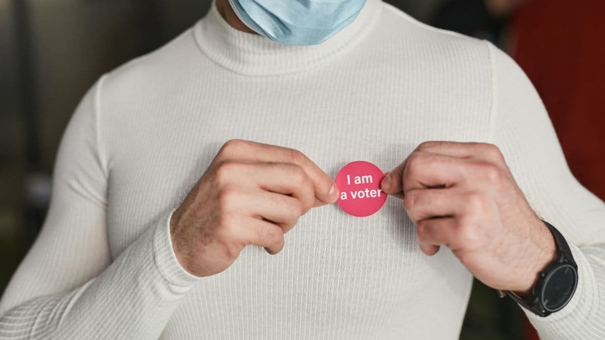 Man in white turtleneck applying an 'I Am A Voter' sticker, signifies civic engagement.