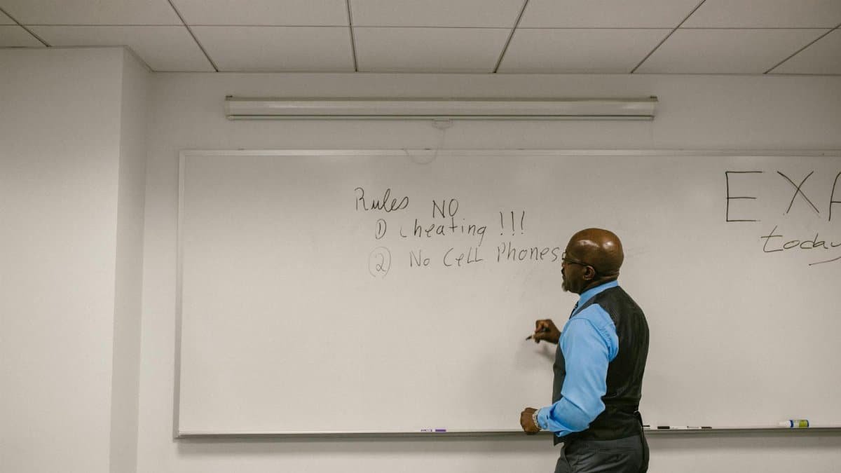 Instructor writing exam rules on a whiteboard in a college classroom.