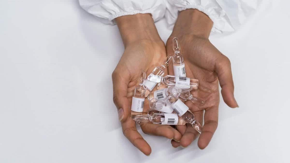 Close-up of hands in protective clothing holding vaccine vials, symbolizing health and safety.