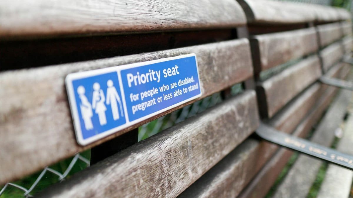 Close-up of a weathered wooden bench with a priority seating sign for disabled, pregnant individuals.
