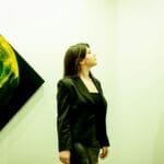 A woman in a black outfit admiring abstract paintings in a modern art gallery.