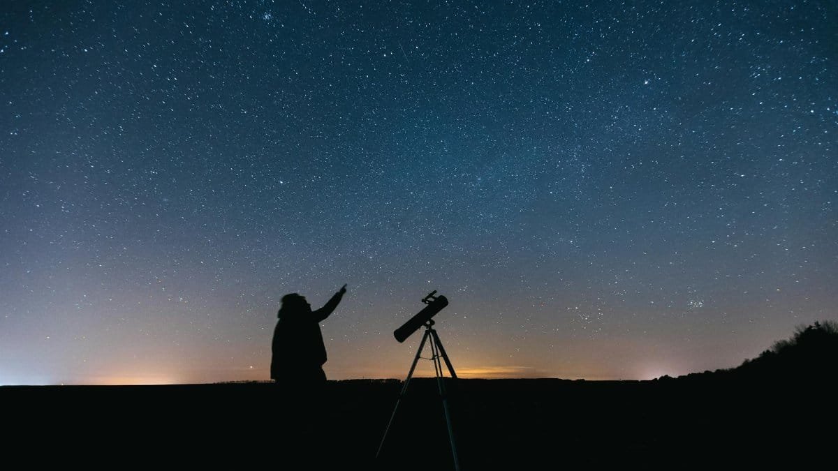 Silhouette of person with telescope gazing at a starry night sky, showcasing celestial beauty.