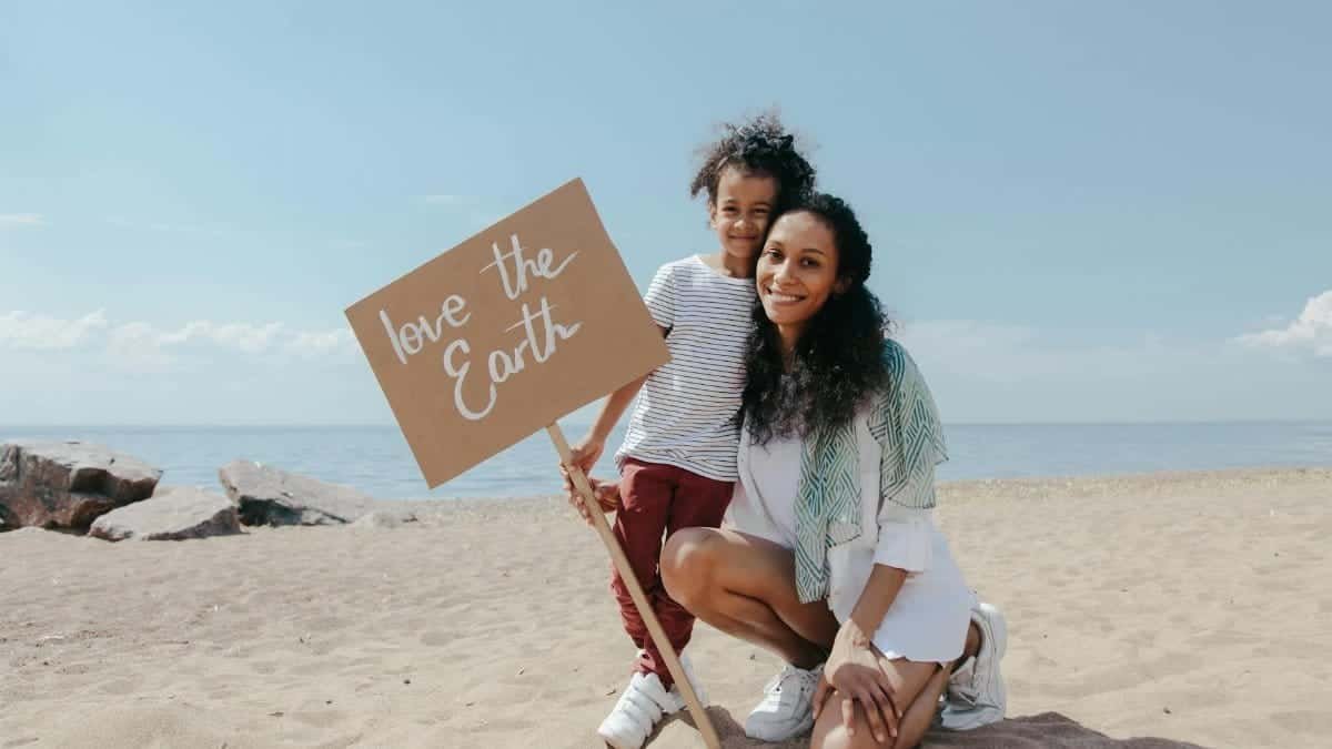 A mother and child holding a 'Love the Earth' sign on a sunny beach, promoting environmental awareness.