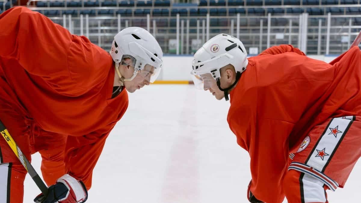 Two ice hockey players in red uniforms preparing for a face-off on the indoor rink.
