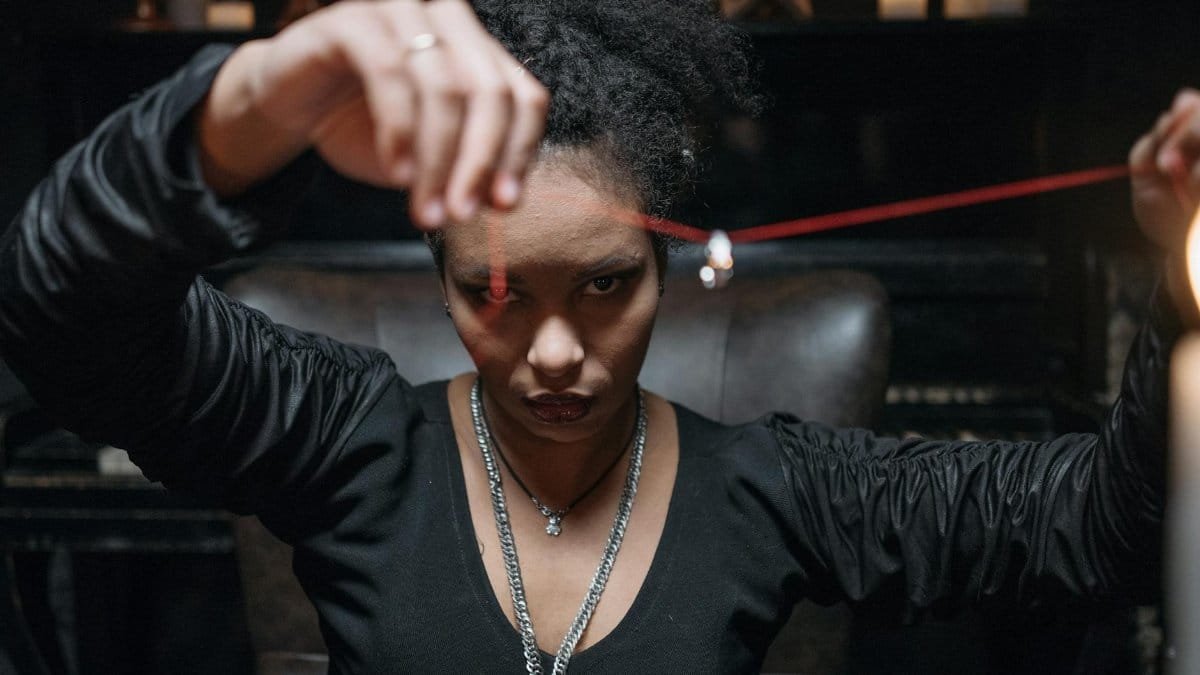 A young woman in a mysterious setting, holding a pendant with intense gaze and dim candlelight.