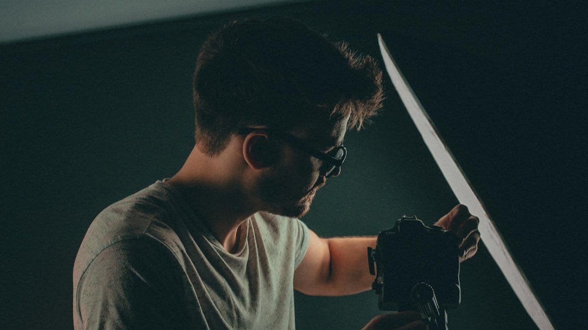 Photographer adjusting camera and equipment in a studio setting. Low light atmosphere.