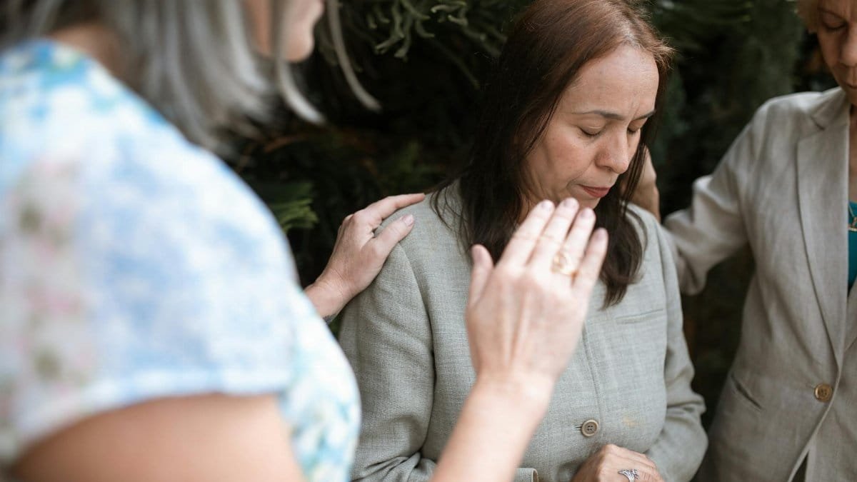 Three women in a heartfelt prayer gathering, emphasizing faith and community.