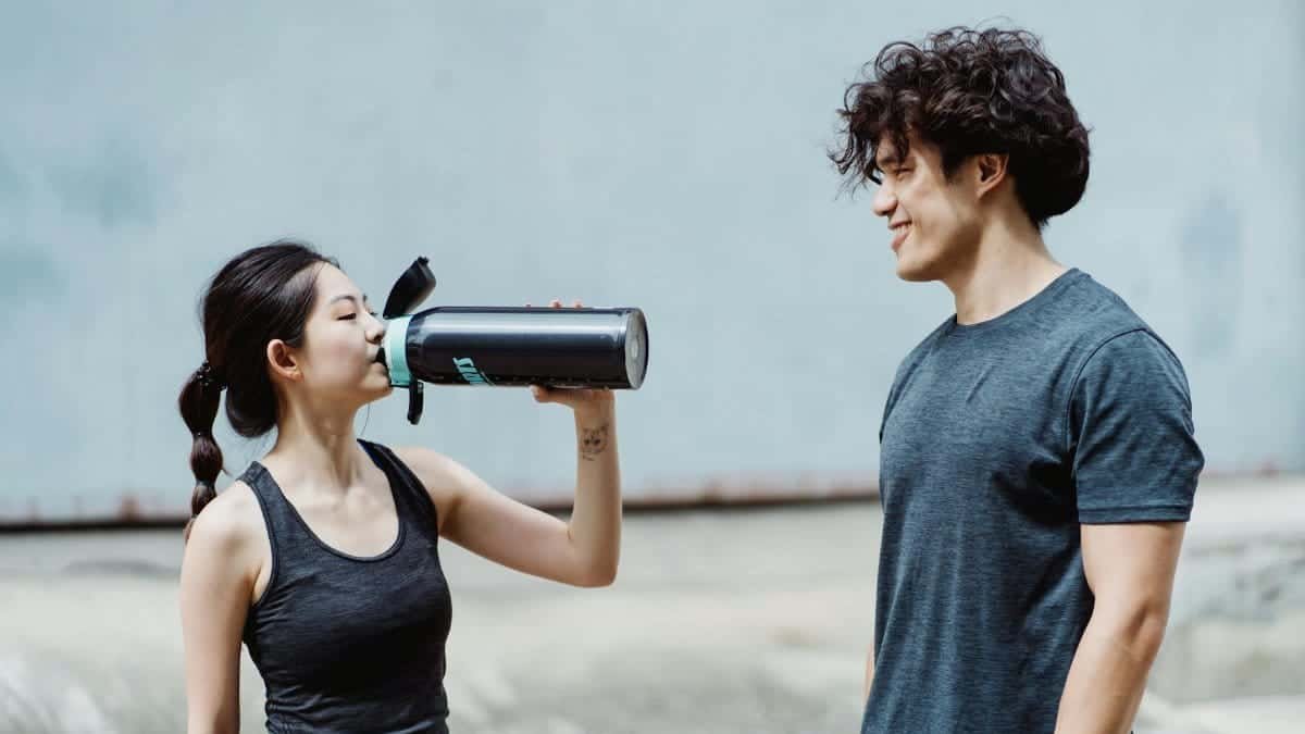 A young man and woman enjoy an outdoor workout session, sharing a moment of hydration and camaraderie.