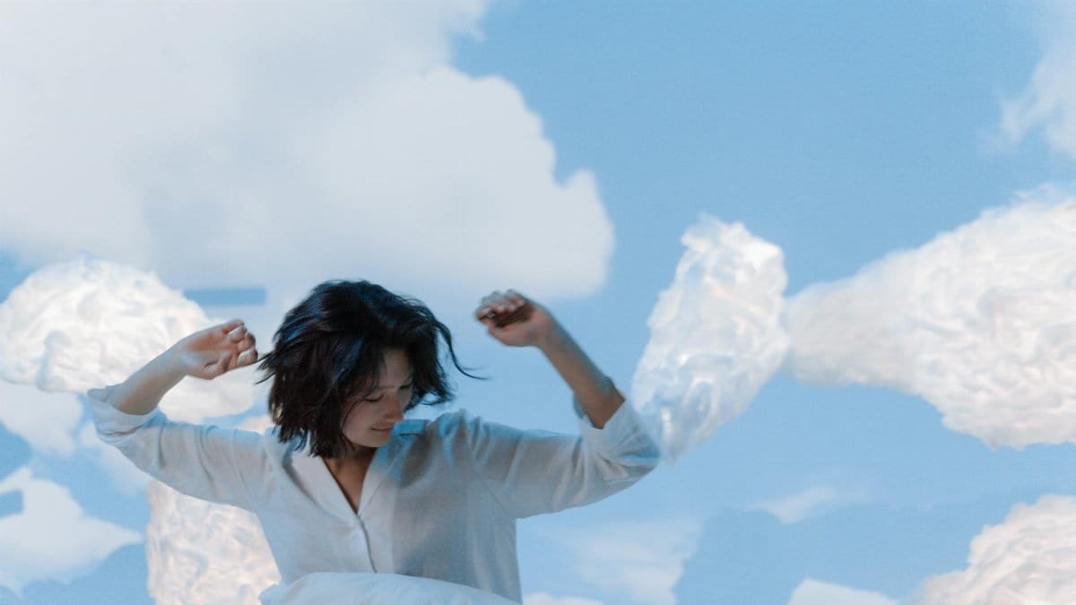 Asian woman with short hair in white shirt surrounded by clouds, evoking peaceful dreaming.