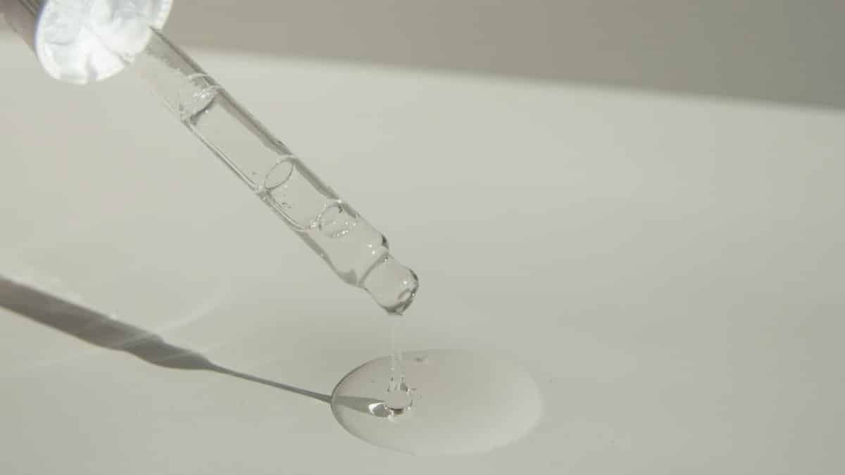 Close-up of a cosmetic pipette releasing serum onto a surface with soft sunlight.