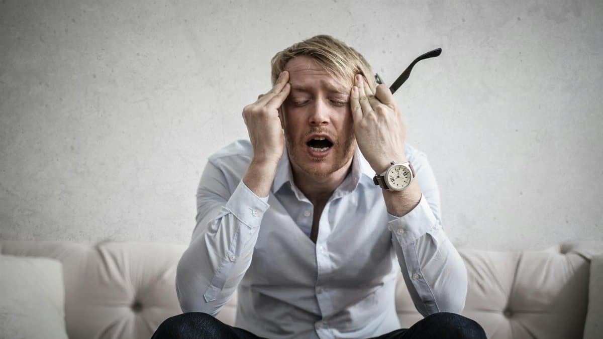 Stressed man sitting on couch, feeling overwhelmed and frustrated, expressing mental strain.