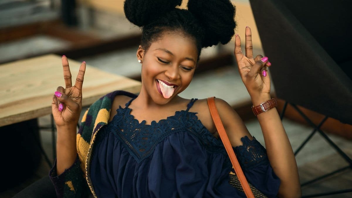 Joyful young woman making peace signs and posing playfully indoors.