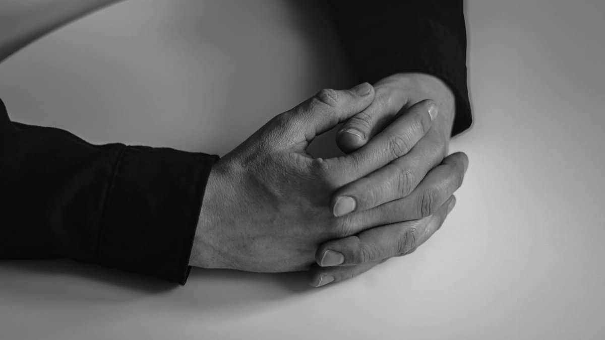 Black and white close-up of hands clasped together, conveying unity and contemplation.