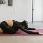 Adult woman using VR headset while performing yoga on a mat in a minimalist indoor setting.